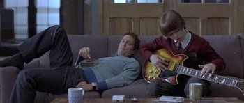 Movie still from “About a Boy” (2002), directed by Chris Weitz – A man laying on a couch next to a boy; Medium shot, Low angle