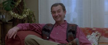Movie still from “About a Boy” (2002), directed by Chris Weitz – A man sitting on a couch wearing glasses and smiling; Close Up shot, Low angle