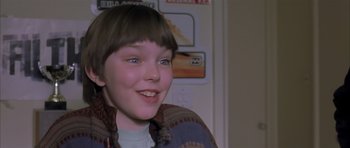 Movie still from “About a Boy” (2002), directed by Chris Weitz – A young boy smiling for the camera in front of a wall; Close Up shot, High angle