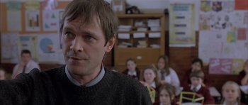 Movie still from “About a Boy” (2002), directed by Chris Weitz – A group of people sitting in a room with a man; Close Up shot, Over the shoulder angle