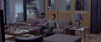 Movie still from “About a Boy” (2002), directed by Chris Weitz – A man sitting on top of a purple couch in a living room; Wide shot, High angle