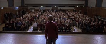 Movie still from “About a Boy” (2002), directed by Chris Weitz – A woman standing in front of a crowd of people; Wide shot, High angle