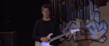 Movie still from “About a Boy” (2002), directed by Chris Weitz – A man holding a white electric guitar in front of a crowd; Medium shot, Low angle