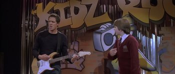 Movie still from “About a Boy” (2002), directed by Chris Weitz – Two young men are playing guitar in front of a graffiti wall; Medium shot, Over the shoulder angle