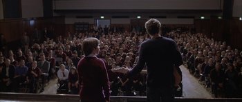 Movie still from “About a Boy” (2002), directed by Chris Weitz – Two people standing in front of an audience holding guitars; Wide shot, Over the shoulder angle