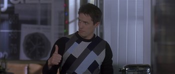 Movie still from “About a Boy” (2002), directed by Chris Weitz – A man giving a thumbs up while wearing a black and white sweater; Medium shot, Low angle