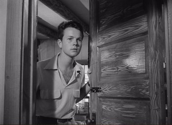 Movie still from “Ace in the Hole” (1951), directed by Billy Wilder – A man standing in front of an open wooden door; Close Up shot, Low angle