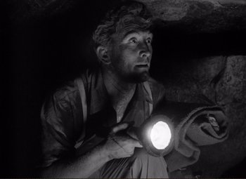 Movie still from “Ace in the Hole” (1951), directed by Billy Wilder – A man is holding a flashlight in a cave; Close Up shot, Low angle
