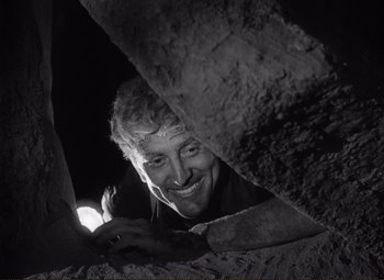 Movie still from “Ace in the Hole” (1951), directed by Billy Wilder – A black - and - white photo of a man looking through a hole; Medium shot, Low angle
