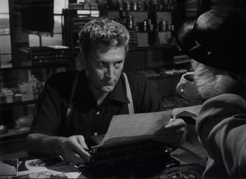 Movie still from “Ace in the Hole” (1951), directed by Billy Wilder – A man sitting at a table looking at a piece of paper; Close Up shot, Over the shoulder angle