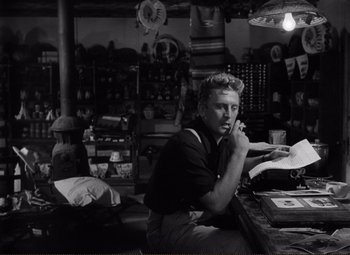 Movie still from “Ace in the Hole” (1951), directed by Billy Wilder – A black and white photo of a man sitting at a table; Medium shot, Low angle
