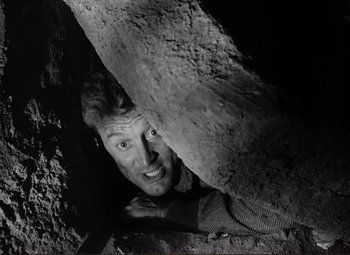 Movie still from “Ace in the Hole” (1951), directed by Billy Wilder – A black and white photo of a man peeking out from a cave; Close Up shot, Overhead angle