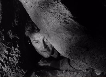 Movie still from “Ace in the Hole” (1951), directed by Billy Wilder – A black - and - white photo of a man peeking out from a cave; Close Up shot, Overhead angle