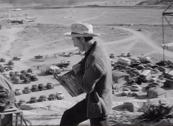 Movie still from “Ace in the Hole” (1951), directed by Billy Wilder – A man in a white hat is holding a newspaper; Wide shot, High angle