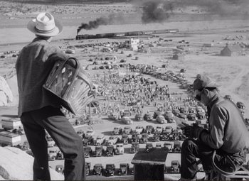 Movie still from “Ace in the Hole” (1951), directed by Billy Wilder – Two men standing on the side of a road looking over a field; Extreme Wide shot, High angle