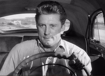 Movie still from “Ace in the Hole” (1951), directed by Billy Wilder – A black and white photo of a man driving a car; Close Up shot, Low angle