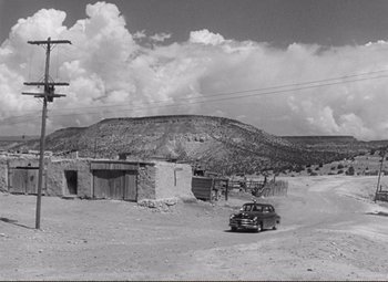 Movie still from “Ace in the Hole” (1951), directed by Billy Wilder – An old black and white photo of a car parked in front of a building; Extreme Wide shot, Low angle