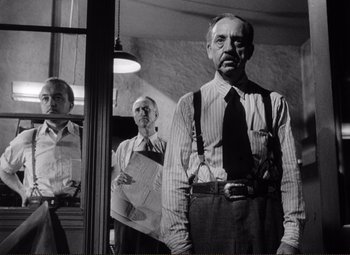 Movie still from “Ace in the Hole” (1951), directed by Billy Wilder – A man standing next to another man in a room; Medium shot, Low angle