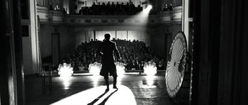 Movie still from “Adam Resurrected” (2008), directed by Paul Schrader – A man standing in front of an audience on a stage; Wide shot, Low angle