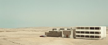 Movie still from “Adam Resurrected” (2008), directed by Paul Schrader – A car is parked in front of a building in the desert; Extreme Wide shot, Low angle