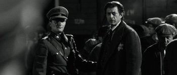 Movie still from “Adam Resurrected” (2008), directed by Paul Schrader – A man in a suit and tie standing next to another man in a suit and tie; Medium shot, Over the shoulder angle