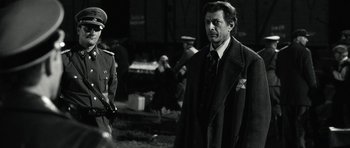 Movie still from “Adam Resurrected” (2008), directed by Paul Schrader – A man in a suit and tie standing next to a man in a tie; Medium shot, Over the shoulder angle