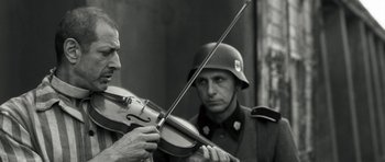 Movie still from “Adam Resurrected” (2008), directed by Paul Schrader – A man playing a violin while another man looks on; Close Up shot, Low angle