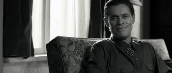 Movie still from “Adam Resurrected” (2008), directed by Paul Schrader – A black and white photo of a man sitting on a couch; Close Up shot, Over the shoulder angle