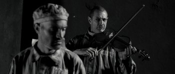 Movie still from “Adam Resurrected” (2008), directed by Paul Schrader – A man holding a violin in front of another man; Close Up shot, Low angle