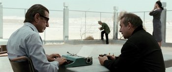 Movie still from “Adam Resurrected” (2008), directed by Paul Schrader – Two men are sitting at a table and one is typing on a typewriter; Wide shot, Over the shoulder angle