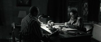 Movie still from “Adam Resurrected” (2008), directed by Paul Schrader – Two men sitting at a table in front of a lamp; Medium shot, Over the shoulder angle