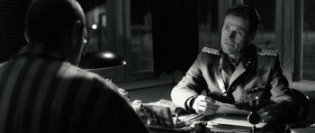 Movie still from “Adam Resurrected” (2008), directed by Paul Schrader – A man sitting at a table in front of a lamp; Close Up shot, Over the shoulder angle