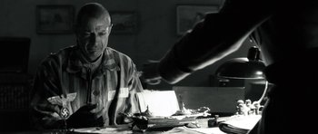 Movie still from “Adam Resurrected” (2008), directed by Paul Schrader – An older man sitting at a table with papers; Medium shot, Over the shoulder angle