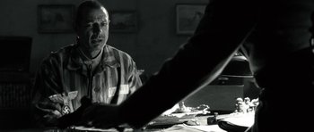 Movie still from “Adam Resurrected” (2008), directed by Paul Schrader – A black and white photo of a man sitting at a table; Medium shot, Over the shoulder angle