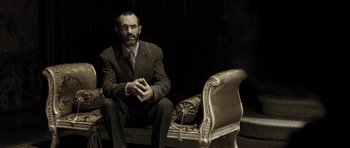 Movie still from “Adam Resurrected” (2008), directed by Paul Schrader – A man in a suit sitting in front of a couch; Medium shot, Low angle