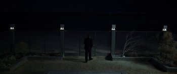 Movie still from “Adam Resurrected” (2008), directed by Paul Schrader – A man standing in front of a fence at night; Extreme Wide shot, Over the shoulder angle