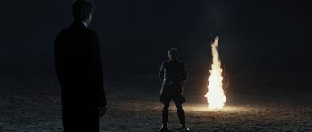 Movie still from “Adam Resurrected” (2008), directed by Paul Schrader – A man standing in front of a fire at night; Wide shot, Over the shoulder angle