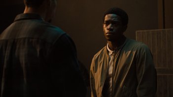 Movie still from “Snowfall” (2017), directed by Hiro Murai – A man standing next to another man in a dark room; Medium shot, Over the shoulder angle
