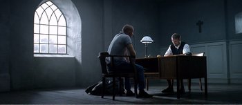 Movie still from “Adam's Apples” (2005), directed by Anders Thomas Jensen – A man sitting on a chair next to another man; Wide shot, Over the shoulder angle