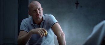 Movie still from “Adam's Apples” (2005), directed by Anders Thomas Jensen – A man holding an apple while sitting down; Close Up shot, Low angle