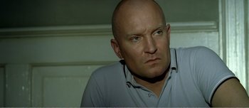 Movie still from “Adam's Apples” (2005), directed by Anders Thomas Jensen – A man with a shaved head and a blue shirt; Close Up shot, Low angle