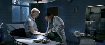 Movie still from “Adam's Apples” (2005), directed by Anders Thomas Jensen – A doctor and a patient in a hospital room; Medium shot, High angle