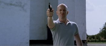 Movie still from “Adam's Apples” (2005), directed by Anders Thomas Jensen – A bald man holding a gun in his right hand; Medium shot, Low angle