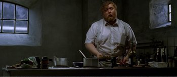 Movie still from “Adam's Apples” (2005), directed by Anders Thomas Jensen – A man standing in front of a table with pans; Medium shot, Low angle