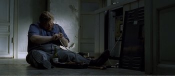 Movie still from “Adam's Apples” (2005), directed by Anders Thomas Jensen – A man sitting on the ground with a bottle of wine; Medium shot, High angle