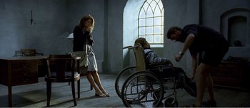 Movie still from “Adam's Apples” (2005), directed by Anders Thomas Jensen – A woman sitting on a chair next to a man in a wheel chair; Wide shot, Low angle
