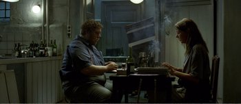 Movie still from “Adam's Apples” (2005), directed by Anders Thomas Jensen – A man sitting at a table with a bottle of wine; Medium shot, Over the shoulder angle