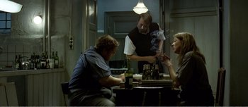 Movie still from “Adam's Apples” (2005), directed by Anders Thomas Jensen – Three people sitting at a table with a bottle of wine; Medium shot, Over the shoulder angle
