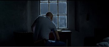 Movie still from “Adam's Apples” (2005), directed by Anders Thomas Jensen – A man sitting in front of a window in a dark room; Medium shot, Low angle