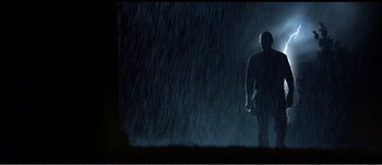 Movie still from “Adam's Apples” (2005), directed by Anders Thomas Jensen – A man standing in the rain holding a phone; Wide shot, Low angle